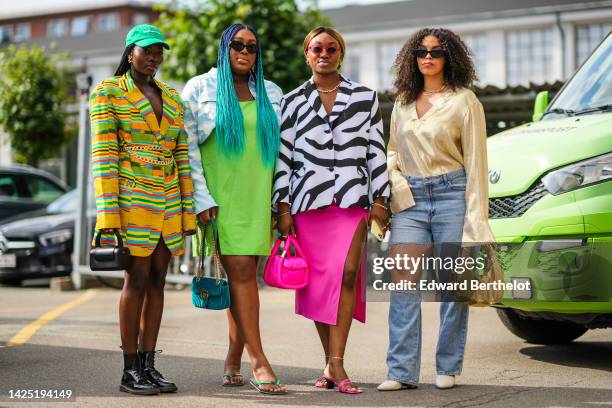 Guest wears a green cap, gold earrings, a yellow with red / blue / green striped print pattern wool blazer jacket, a gold large chain belt, a black...