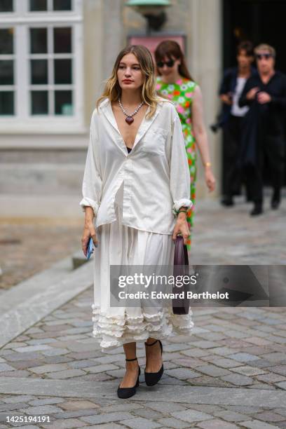 Guest wears a silver and white pearls with brown heart pendant stone necklace, a white striped print pattern shirt, a white latte tulle / ruffled...