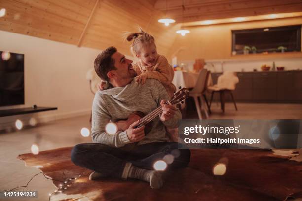 young cheerful dad sitting with his daughter in living room and playing on guitar. - fabolous musician bildbanksfoton och bilder