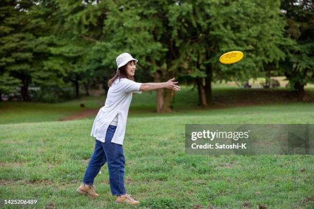 mother throwing flying disc in green field in public park - throwing stock pictures, royalty-free photos & images