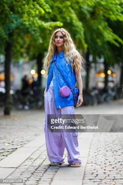Emili Sindlev wears a royal blue quilted / sleeveless / oversized zipper gilet, a white sleeveless t-shirt, pale purple large cargo pants, a purple...