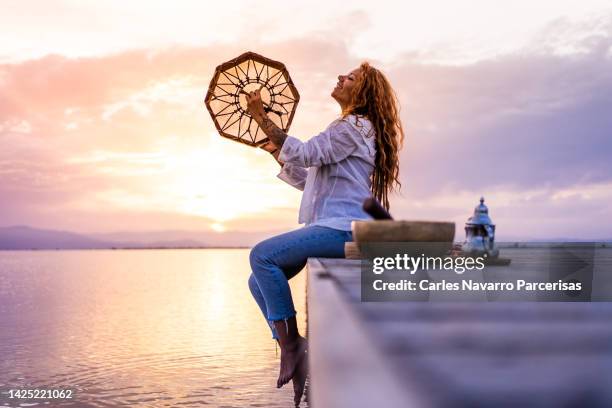 alternative woman doing a spiritual ritual on a lake during sunset - ceremonia fotografías e imágenes de stock