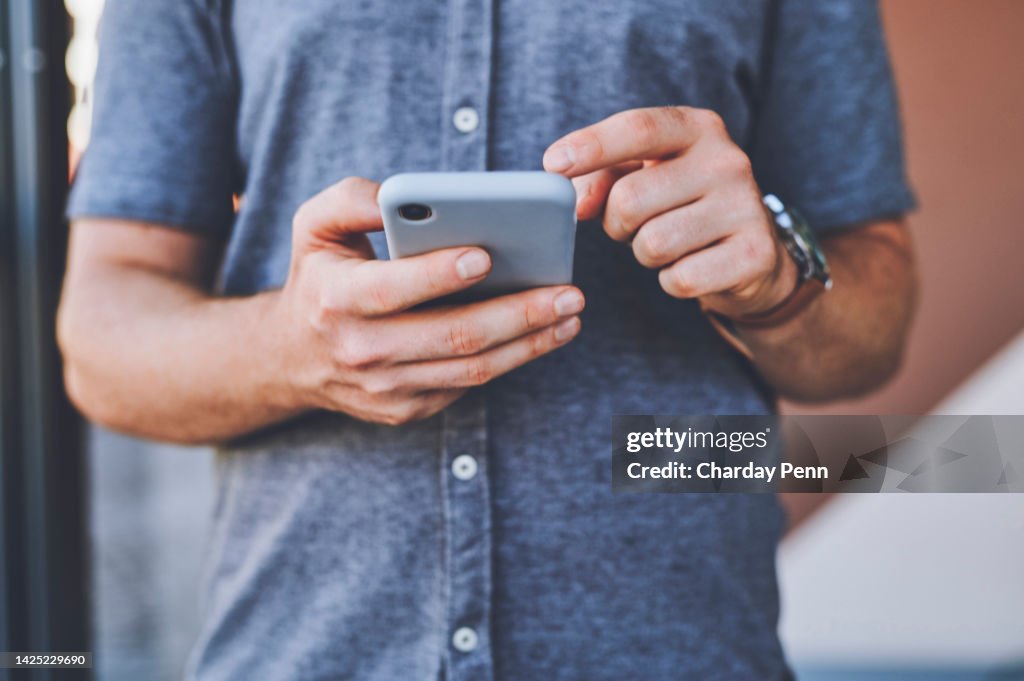 Closeup of man hands on a phone browsing on social media while standing outdoors in the city street. Guy reading an article or blog on a website with a smartphone in an urban town road.