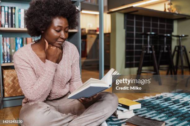 young african-american woman reading a book at home on the floor - woman author stock pictures, royalty-free photos & images