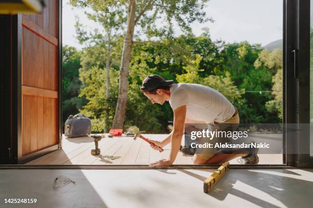 man working on wooden decking in front of a cabin house - hemrenovering bildbanksfoton och bilder