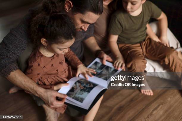 family sitting on the floor looking in photo album - photo album stock pictures, royalty-free photos & images