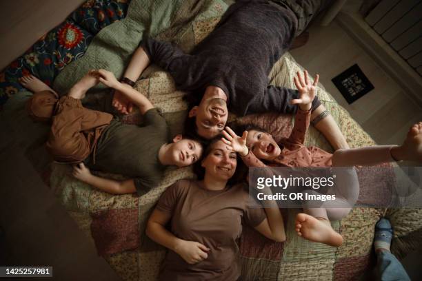 happy family of four lying on bed at home - four people stock pictures, royalty-free photos & images