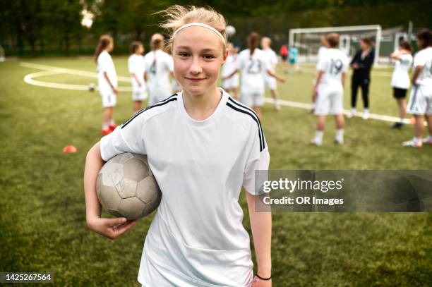 portrait of teenage girl holding ball with soccer team in background - tenue de football photos et images de collection