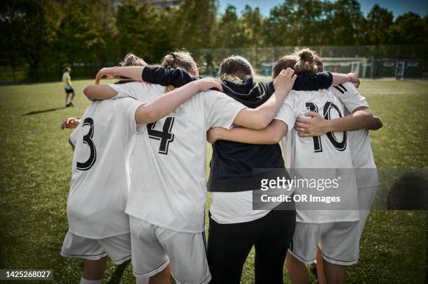 teenage girl soccer team huddling with coach on sports field - soccer team stock pictures, royalty-free photos & images
