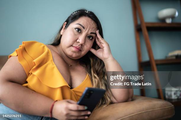 portrait of worried mid adult woman using mobile phone in the living room at home - mobile sad imagens e fotografias de stock