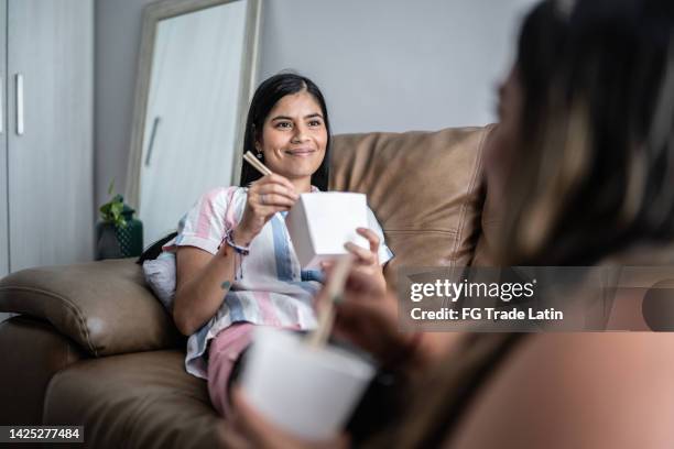 mid adult woman eating yakisoba with her friend in the living room at home - chinese takeout stock pictures, royalty-free photos & images