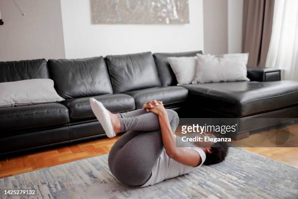 beautiful young woman wearing sportswear practicing yoga, relaxing in knees to chest pose, doing apanasana exercise, sporty girl working out at home - leg stretch girl stock pictures, royalty-free photos & images