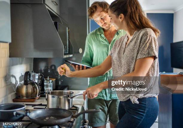 couple using an online recipe to make dinner at home - stove top stock pictures, royalty-free photos & images