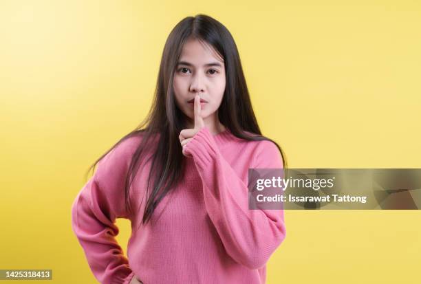 index finger on lips, silence gesture, shhh quiet, asks for voicelessness forefinger at the mouth. young attractive woman in a light t-shirt on yellow background - shhh finger stock pictures, royalty-free photos & images