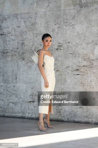 Heart Evangelista wears a bejeweled necklace, a white off-shoulder midi slit dress, a Fendi bag, high heels shoes, during a street style fashion...
