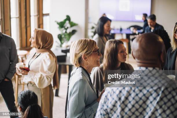 smiling mature businesswoman having coffee with colleagues in break at convention center - meet and greet stock-fotos und bilder