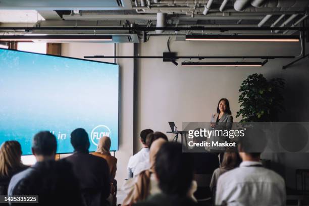 mature businesswoman giving presentation to male and female colleagues in convention center - panel discussion stock pictures, royalty-free photos & images