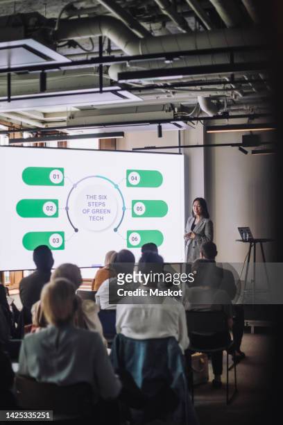 mature female entrepreneur explaining steps of green tech to colleagues during meeting at convention center - women podium stock-fotos und bilder