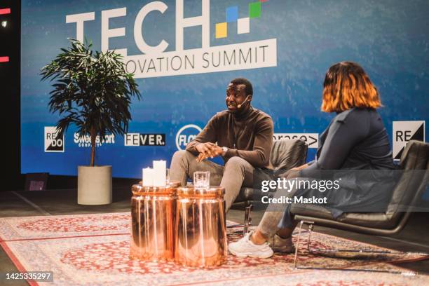 male tech entrepreneur talking with interviewer on stage during conference event - panel stage stock pictures, royalty-free photos & images
