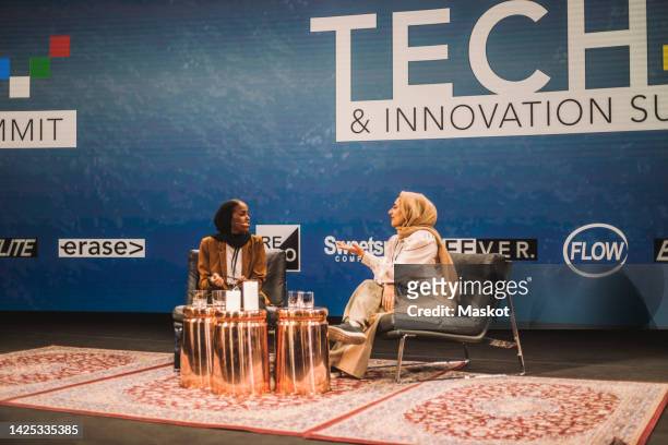 female tech entrepreneur talking with interviewer while sitting on stage during conference event - conference stage stock pictures, royalty-free photos & images