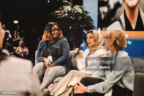 smiling female entrepreneur looking at colleague interacting with interviewer during panel in convention center - entrevista evento imagens e fotografias de stock