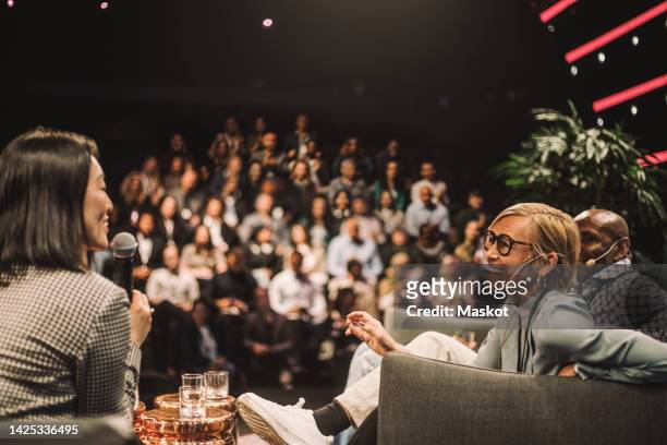 interviewer interacting with smiling entrepreneurs during panel discussion at conference event - business conference - fotografias e filmes do acervo