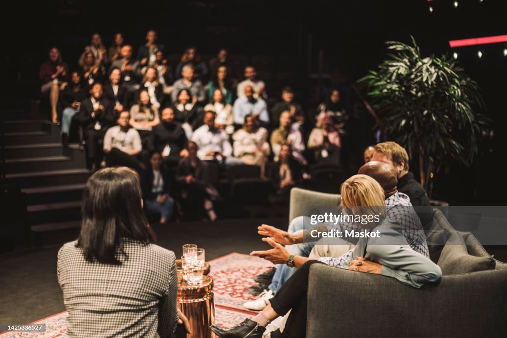 Tech entrepreneurs talking by interviewer during panel discussion at convention center