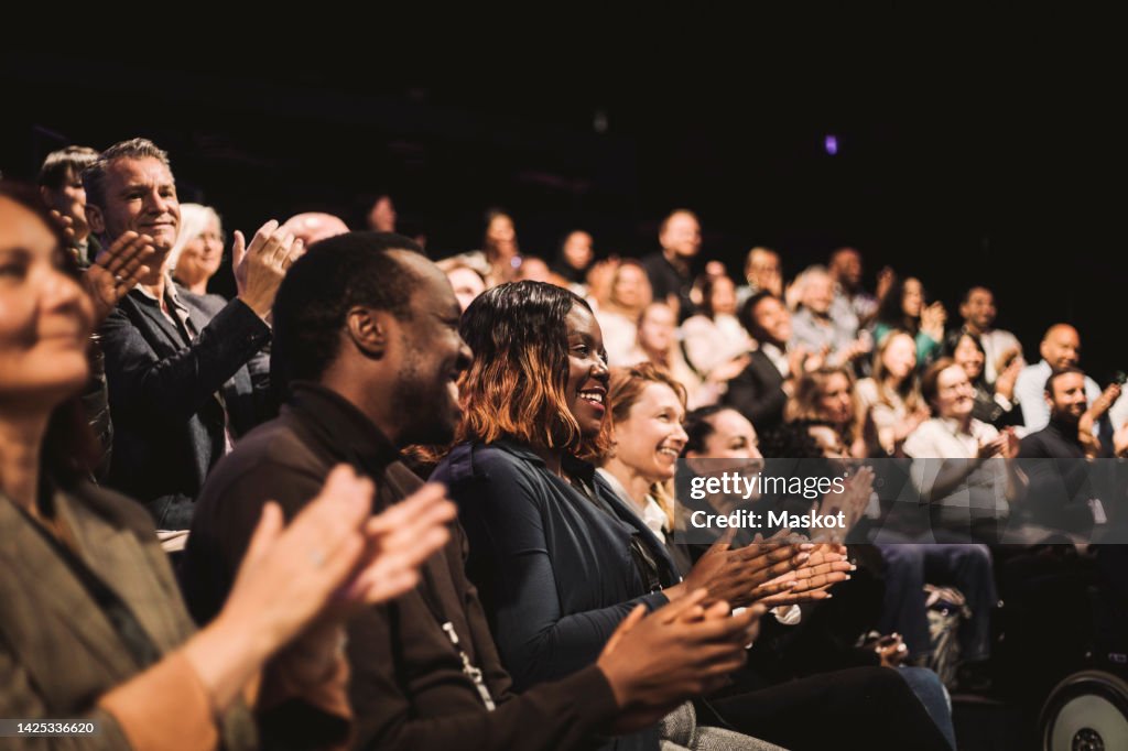 Smiling business colleagues applauding during conference event at convention center