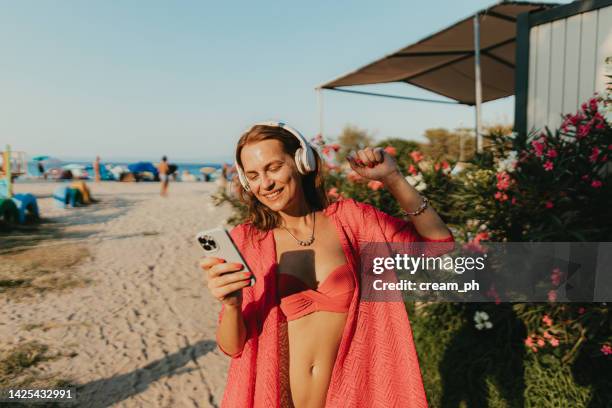 happy woman using a smartphone and listening to music at the beach - beach music stock pictures, royalty-free photos & images