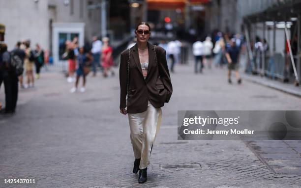 Fashion Week Guest seen wearing a brown blazer, beige long skirt, a white bralette, brown sunglasses, and black overknees boots outside Bevza, during...