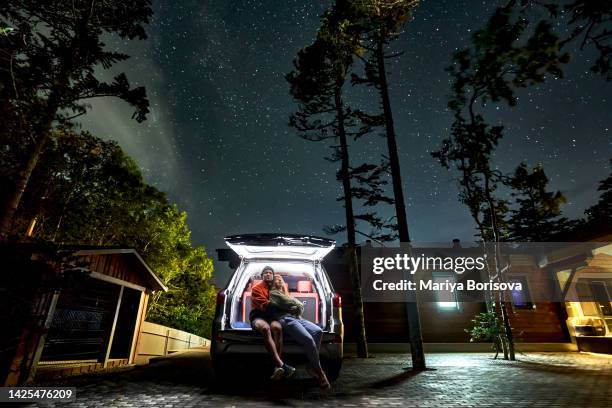 a young couple is sitting in the trunk of a car in an embrace under the night starry sky. - travel boundless stock-fotos und bilder