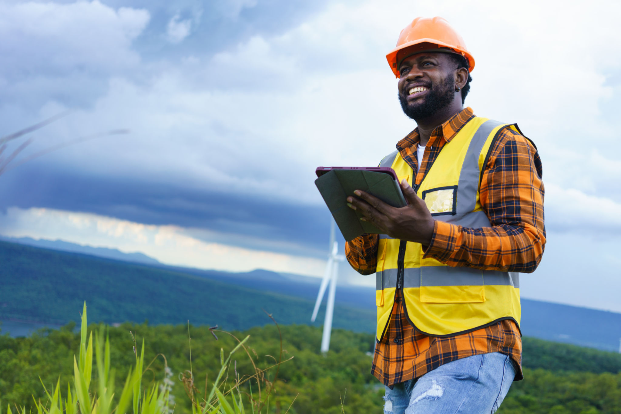 Engenheiro Preto usando jaqueta de segurança e tablet de couro rígido enquanto trabalha no estilo de vida de trabalho ao ar livre e inteligente. Engenheiro Preto usando jaqueta de segurança e tablet de couro rígido enquanto trabalha no estilo de vida de trabalho ao ar livre e inteligente.