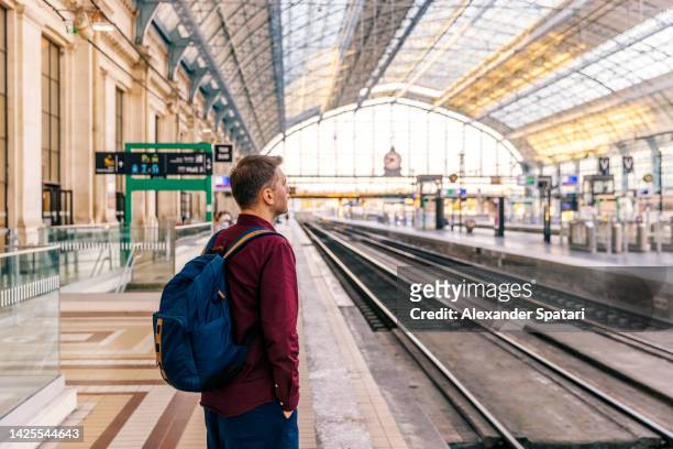 man waiting for a train at the train station, side view - treinstation stockfoto's en -beelden