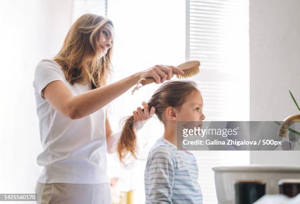young mother with little girl daughter in pajamas combs her hair on morning in bathroom at home - brushing hair stock pictures, royalty-free photos & images