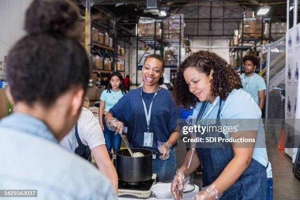 la donna sorride all'amica mentre prepara il cibo per gli affamati - raccolta alimentare foto e immagini stock