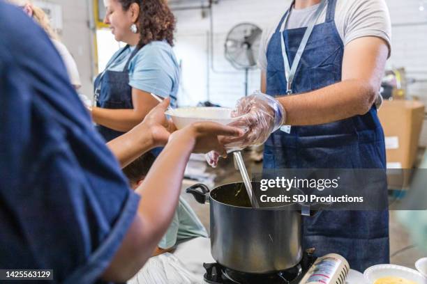 focus on man giving soup to hungry woman - soup kitchen stock pictures, royalty-free photos & images