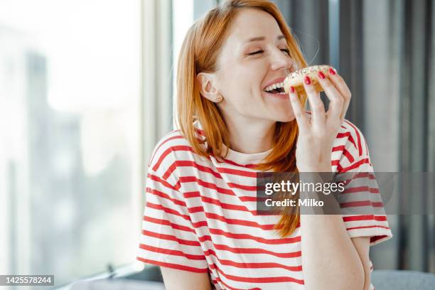portrait of a beautiful woman enjoying eating a doughnut - tårta bildbanksfoton och bilder