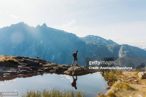 seitenansicht eines mannes mit rucksack, der am sonnigen herbsttag in den bergen norwegens wandert - walking side view stock-fotos und bilder