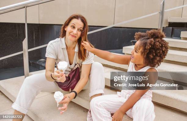 afro girl plays and pulls her white mother's hair while they enjoy eating ice cream of nothing - child pulling hair stock pictures, royalty-free photos & images