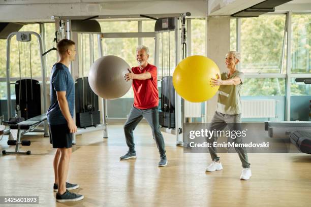 personal trainer helping senior couple exercising with fitness ball at gym - fitness ball stock pictures, royalty-free photos & images