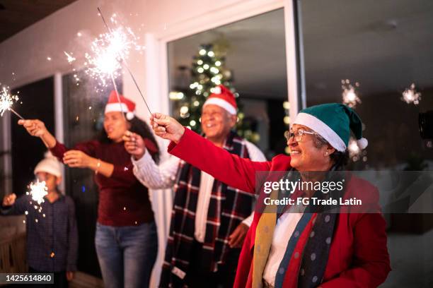 senior woman with family celebrating christmas with sparklers at home - mexican christmas stock pictures, royalty-free photos & images