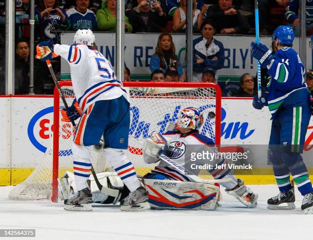 Jeff Petry of the Edmonton Oilers and Alex Burrows of the Vancouver Canucks watch the puck go behind Devan Dubnyk of the Oilers for a goal during...