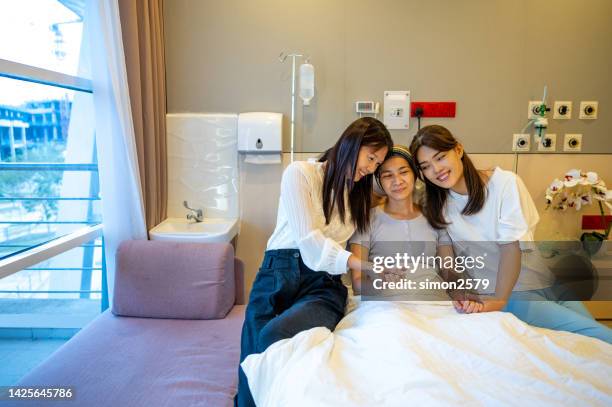 two asian female friends visiting patient in hospital ward. an asian chinese female patient lying on the bed with her two female friends visiting her in the hospital ward - cancer patient with family stock pictures, royalty-free photos & images