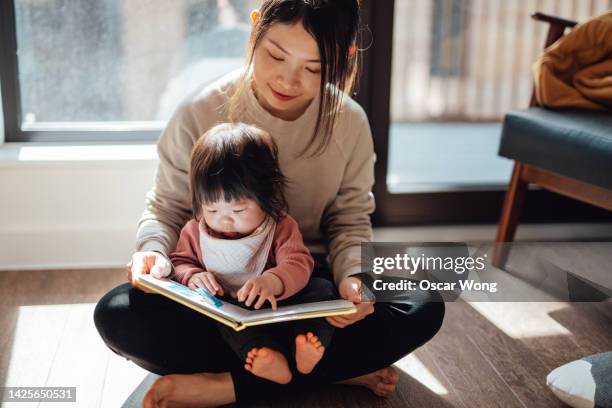 cute asian toddler reading storybook with her mother - family hugging bright stockfoto's en -beelden