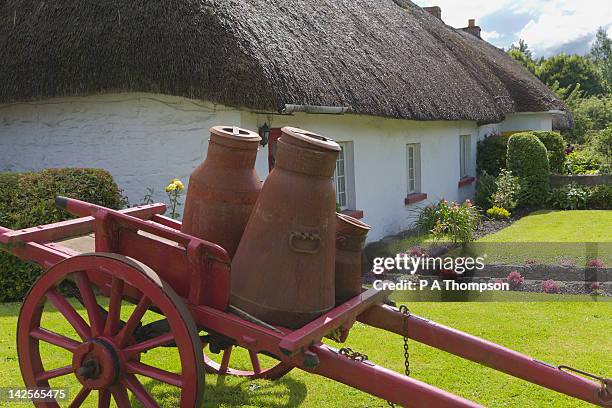 milk churns on a wooden cart outside thatched cottage, adare, county limerick, ireland - vintage butter churn stock pictures, royalty-free photos & images