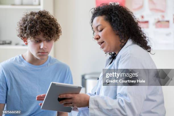 pediatra che mostra al suo paziente adolescente come accedere alle sue cartelle cliniche su un tablet digitale. - 18 19 anni foto e immagini stock