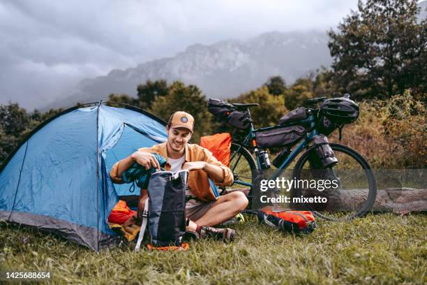 young handsome hiker unloading his backpack in front of his tent - unloading stock pictures, royalty-free photos & images