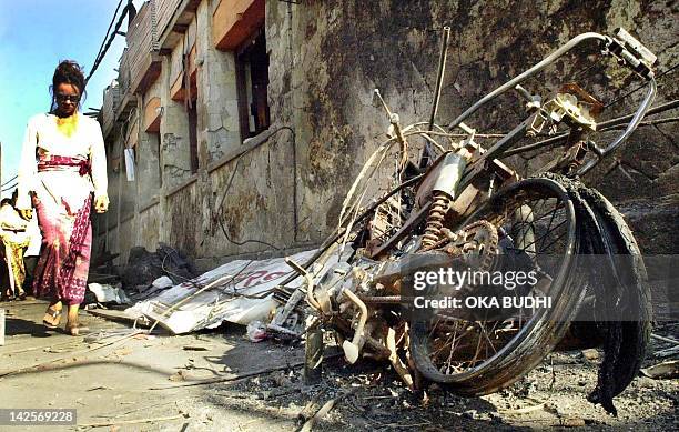 Woman walks past a bomb damaged motorcycle near the blast site at the tourist area of Kuta, Denpasar 18 October 2002. More than 180 were killed 12...