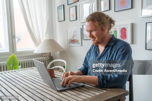 man works on laptop at dining room table - navy blue living room stock pictures, royalty-free photos & images