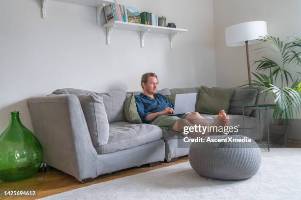 man works on laptop on sofa - navy blue living room stock pictures, royalty-free photos & images